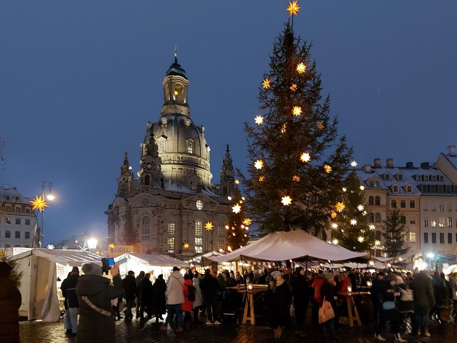 Illuminated Frauenkirche and a starlit Christmas tree above the crowded Advent market on Dresden's Neumarkt at night.