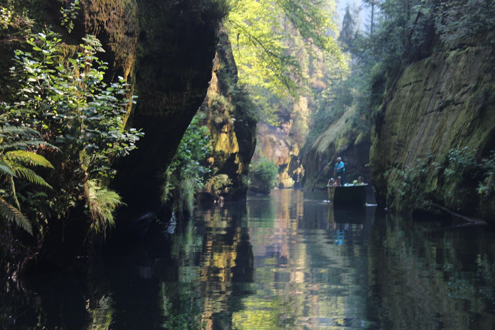 A flat wooden boat on the calm Kamenice river between mossy sandstone walls in Edmund's Gorge