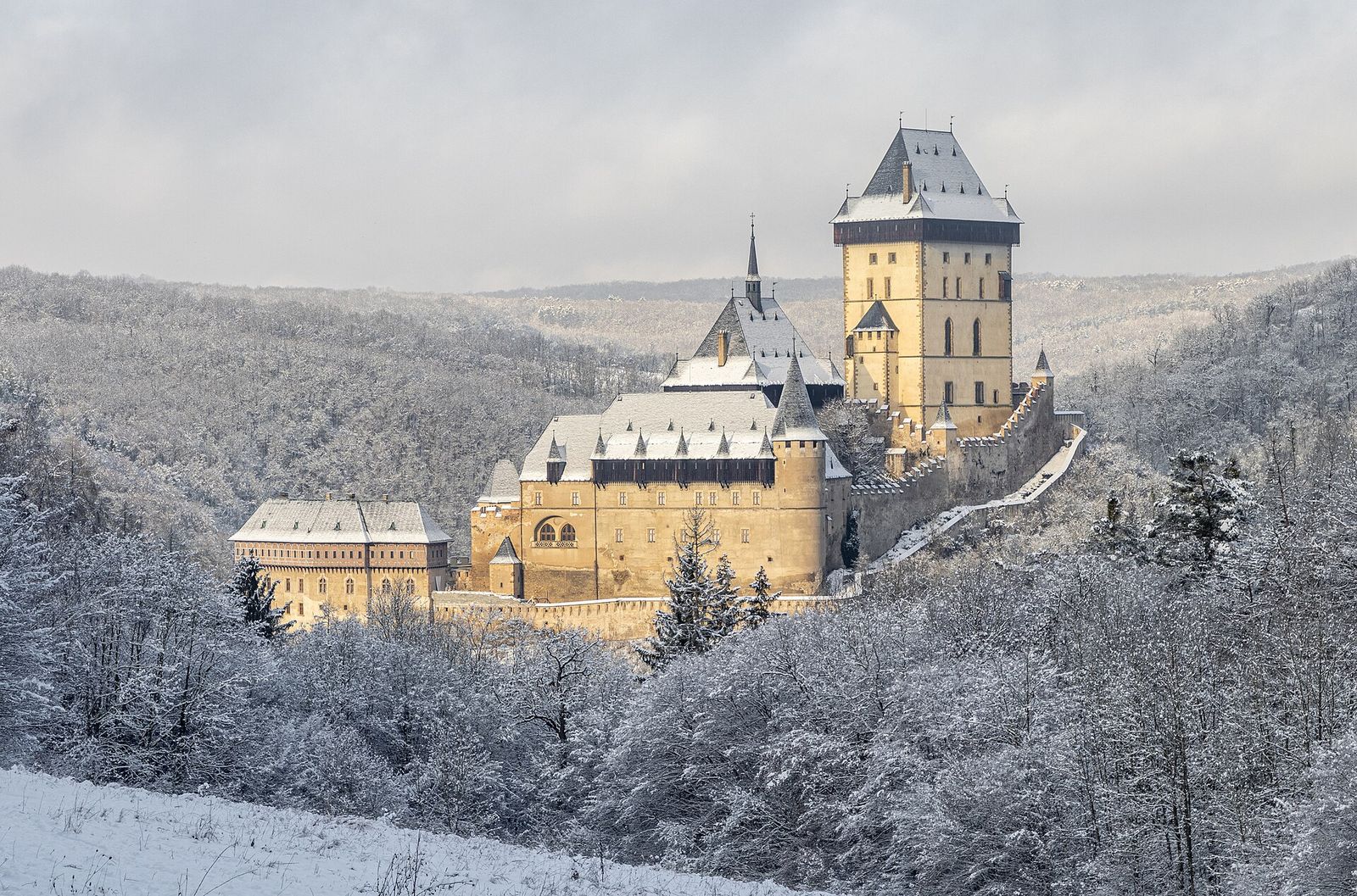 Karlštejn Castle above a frosted, snow-covered forest in winter