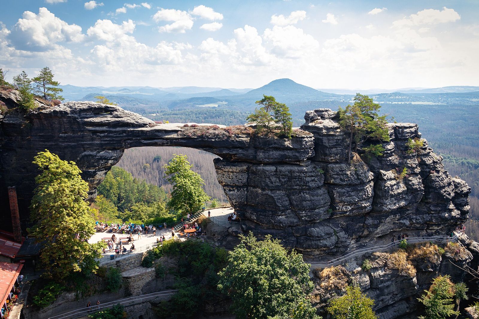 Pravčická Gate and the viewing terrace below it, seen from above, with the forests of the national park beyond